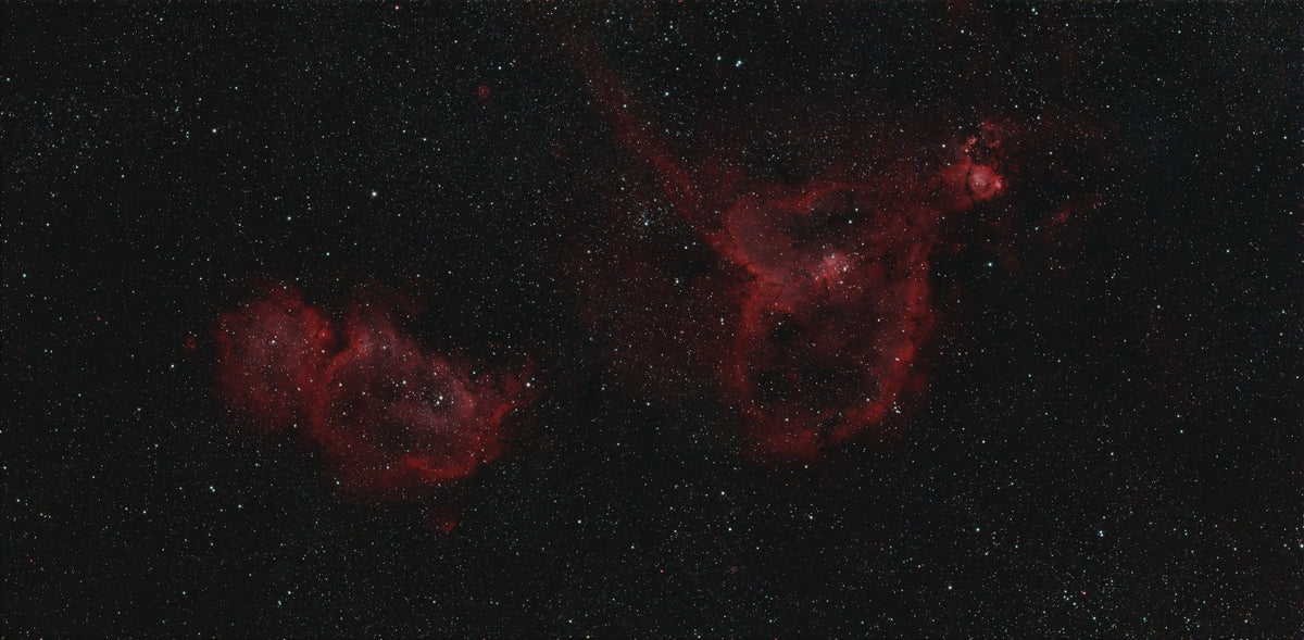 A deep space scene showing two red nebula clouds among numerous small white stars on a black background.