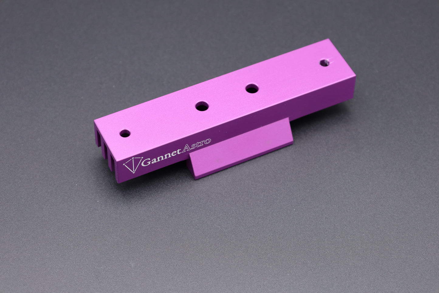A bright purple anodized aluminum Gannet Astro mounting bracket with four screw holes and a white printed logo, shown on a dark gray textured background.