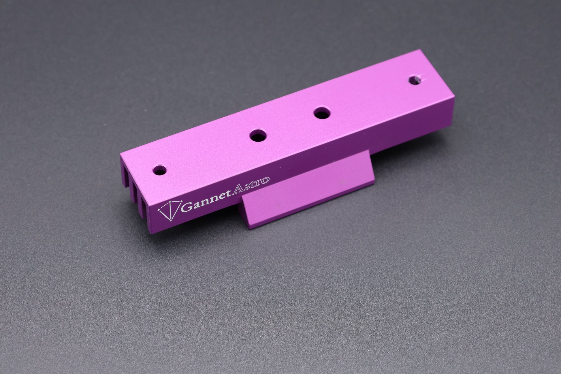 A bright purple anodized aluminum Gannet Astro mounting bracket with four screw holes and a white printed logo, shown on a dark gray textured background.