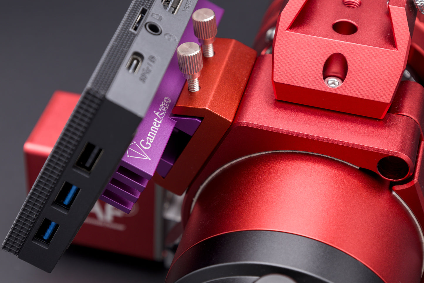 Close-up of a mini PC mounted to the Gannet Astro mounting bracket, attached to a telescope.  The computer is black, the bracket is purple, the telescope is red.