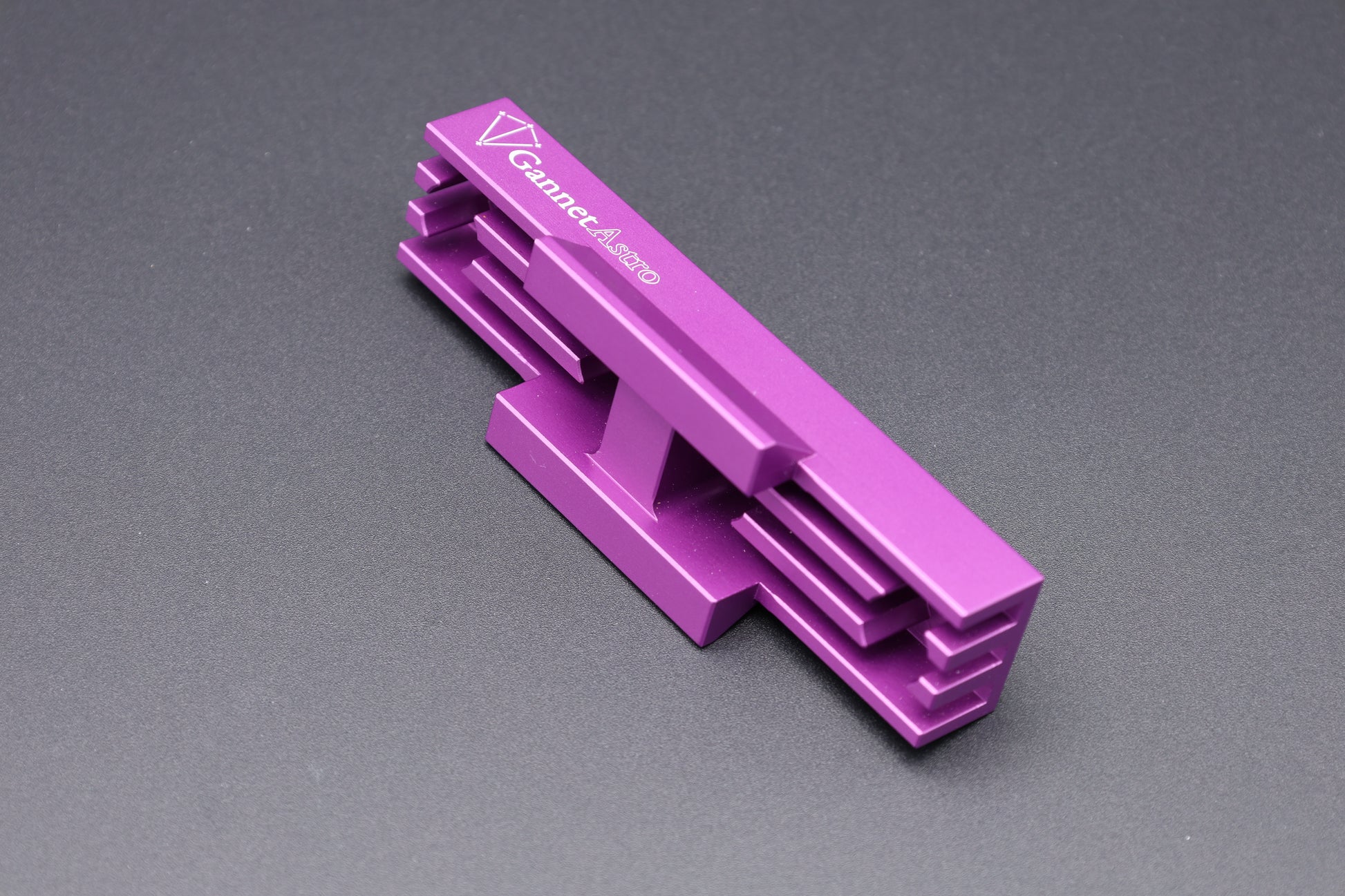 A bright purple anodized aluminum Gannet Astro mounting bracket with a white printed logo, tipped on its side, showing cooling fins and mounting dovetail, on a dark gray textured background.